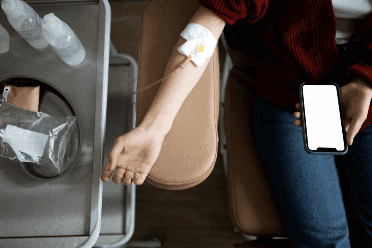 A patient receiving IV treatment while holding a smartphone with a blank screen.
