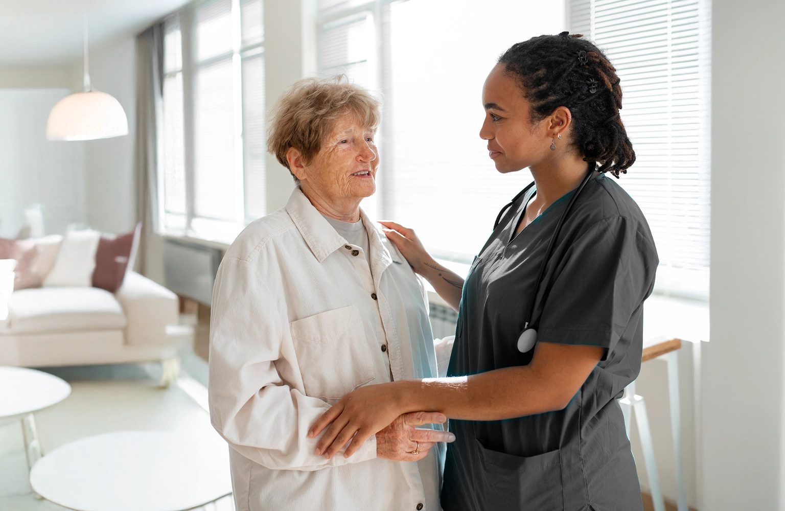 Nurse comforting elderly woman at home during palliative care visit
